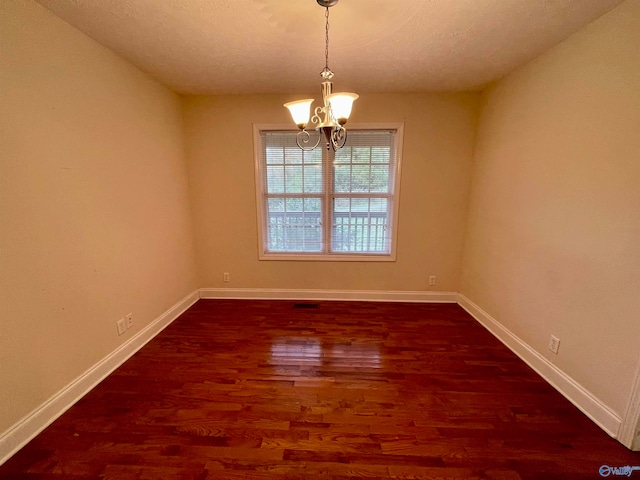 unfurnished room featuring dark wood-type flooring, a textured ceiling, and a notable chandelier