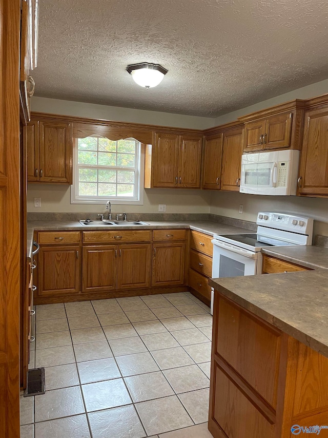 kitchen with a textured ceiling, sink, white appliances, and light tile patterned floors