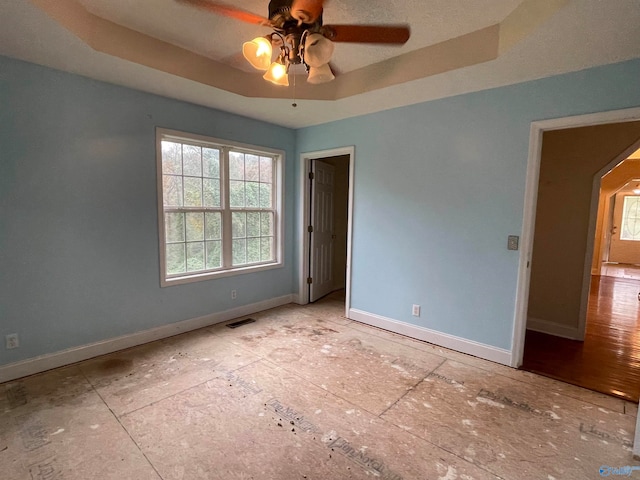 unfurnished bedroom with light wood-type flooring, ceiling fan, and a tray ceiling