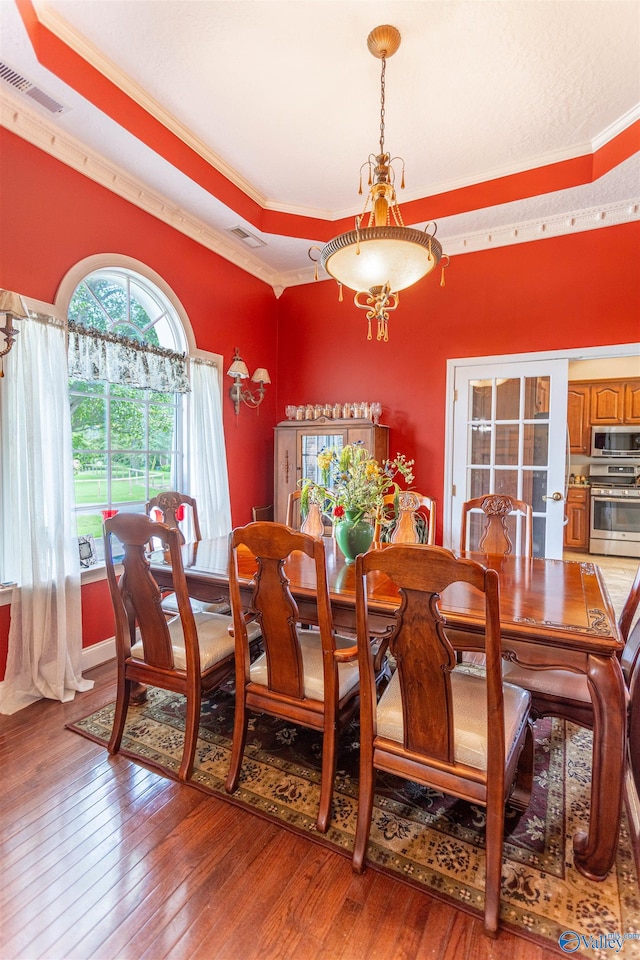 dining room with ornamental molding, wood-type flooring, and a tray ceiling