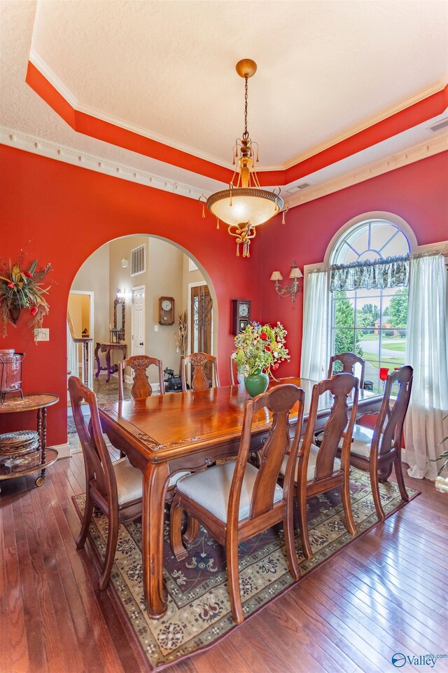 dining space with ornamental molding, wood-type flooring, and a tray ceiling