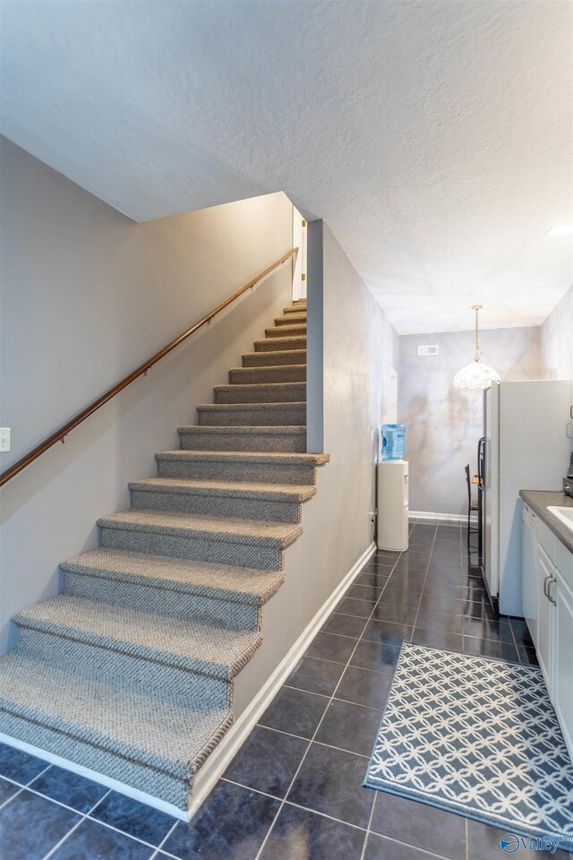 stairway with dark tile patterned floors and a textured ceiling