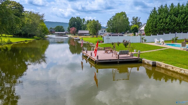 view of dock with a water view, a fenced in pool, and a lawn