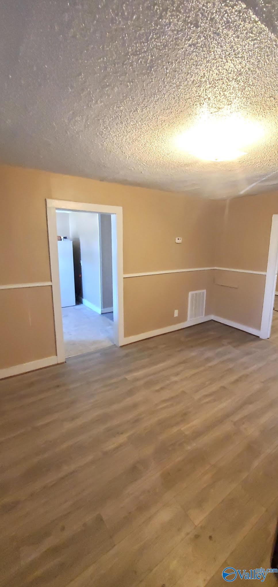 unfurnished room featuring baseboards, wood finished floors, visible vents, and a textured ceiling