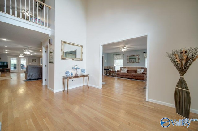 hall with a high ceiling, light wood-style flooring, and baseboards