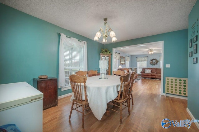 dining space featuring baseboards, light wood-style flooring, a textured ceiling, and ceiling fan with notable chandelier