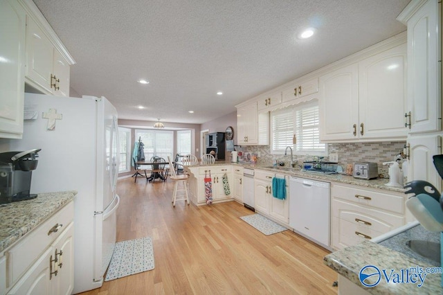 kitchen with light wood finished floors, tasteful backsplash, a sink, white appliances, and a peninsula