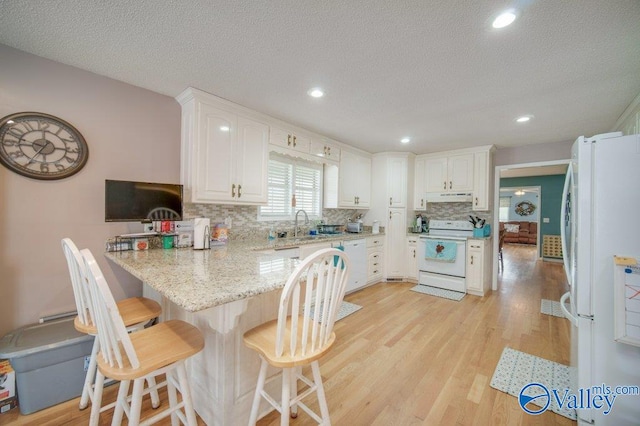 kitchen featuring white appliances, a kitchen breakfast bar, a peninsula, light wood-type flooring, and under cabinet range hood