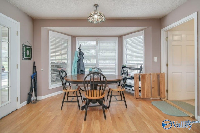 dining space featuring light wood-type flooring, baseboards, and a textured ceiling