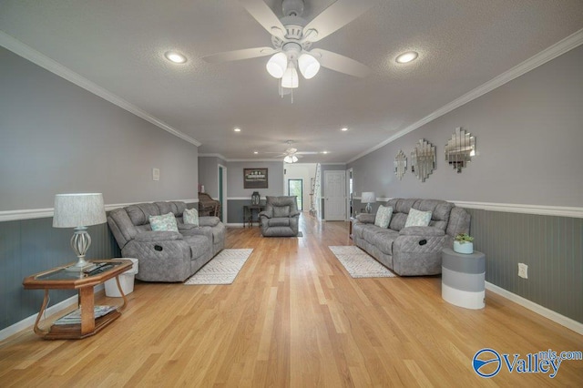 living area with ornamental molding, light wood finished floors, a textured ceiling, and wainscoting