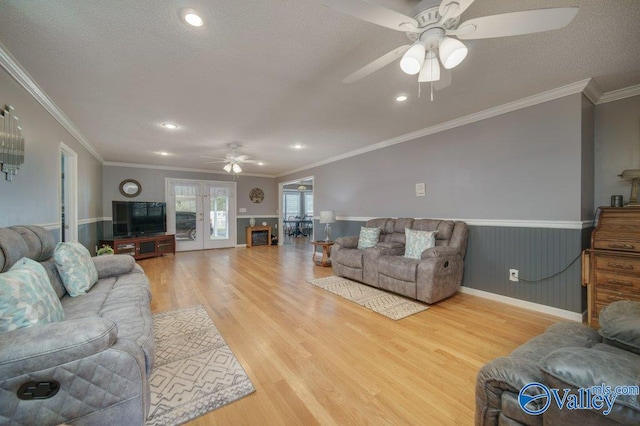 living area with crown molding, a ceiling fan, wainscoting, a textured ceiling, and wood finished floors