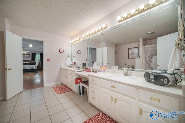 bathroom with a textured ceiling, ensuite bath, vanity, tile patterned flooring, and baseboards