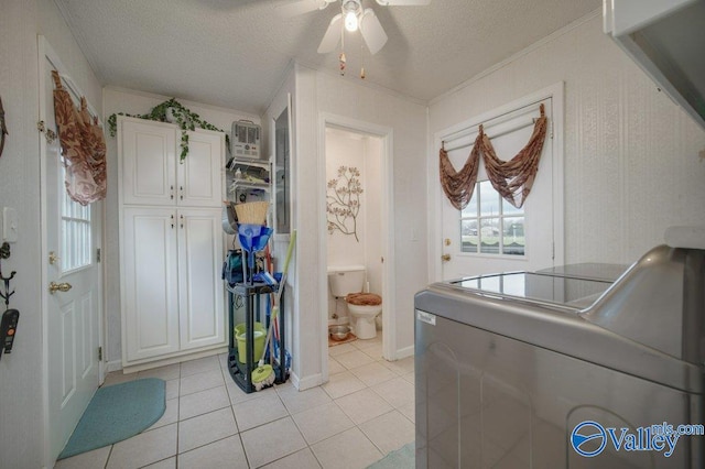 laundry room with a textured ceiling, light tile patterned floors, separate washer and dryer, ornamental molding, and cabinet space