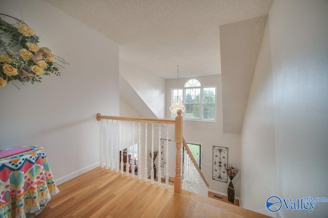 interior space with baseboards, a towering ceiling, wood finished floors, an inviting chandelier, and a textured ceiling