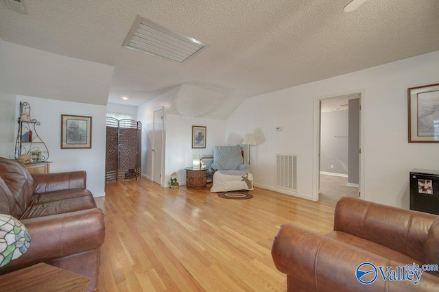 living area with a textured ceiling, light wood finished floors, and visible vents