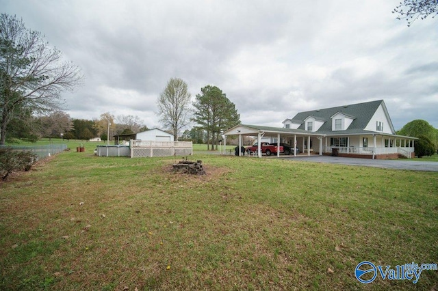 view of yard featuring a carport, an outdoor fire pit, driveway, and fence