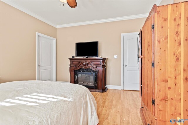 bedroom with light wood-style flooring, ornamental molding, baseboards, and a glass covered fireplace