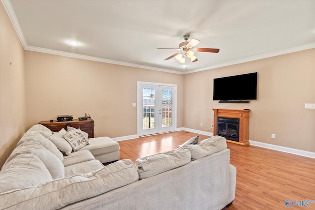 living area with a fireplace, crown molding, light wood-style floors, ceiling fan, and baseboards