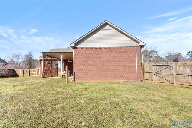 back of house featuring a lawn, a fenced backyard, ceiling fan, a gate, and brick siding