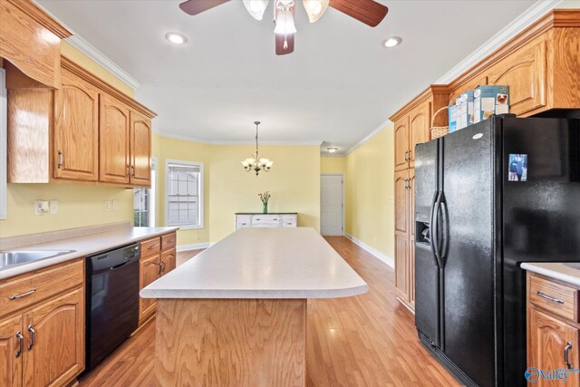 kitchen featuring light countertops, ornamental molding, a center island, black appliances, and light wood finished floors