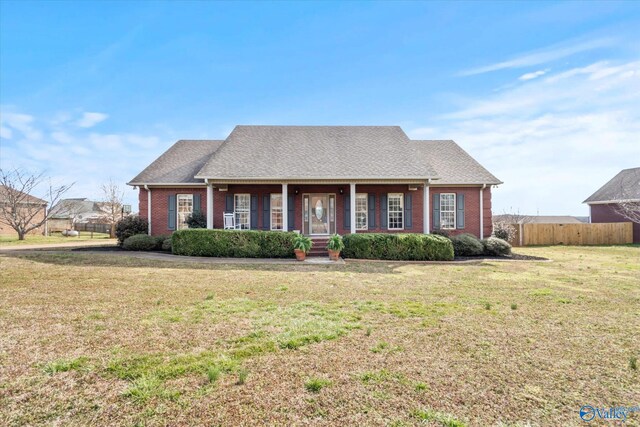 view of front of property with a shingled roof, fence, a front lawn, and brick siding