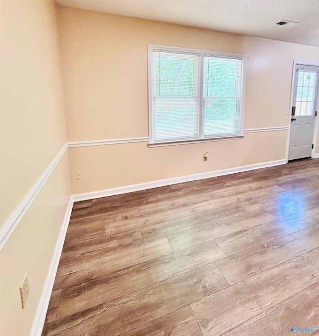 spare room with a textured ceiling, visible vents, wood finished floors, and baseboards