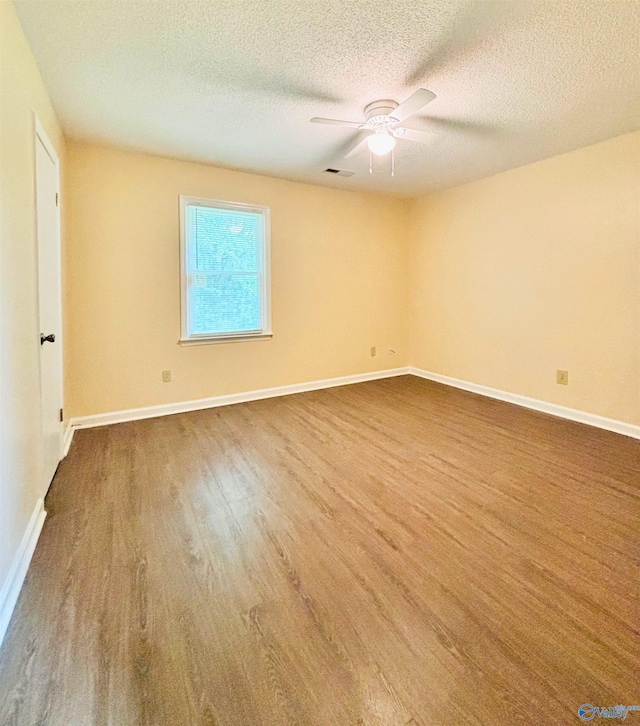 spare room featuring wood finished floors, a ceiling fan, a textured ceiling, visible vents, and baseboards