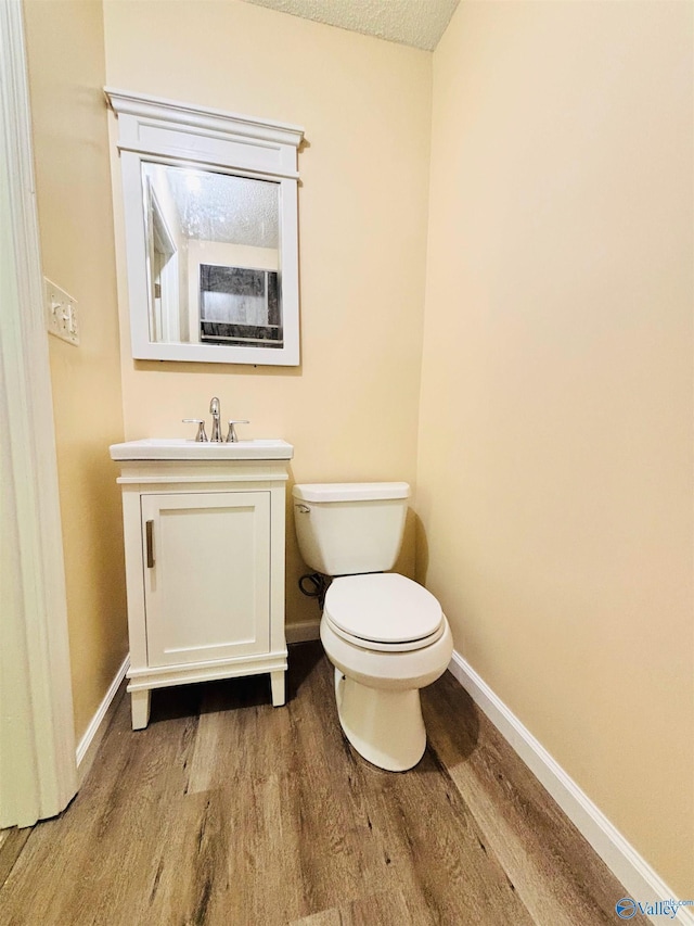 half bathroom with baseboards, vanity, toilet, and wood finished floors