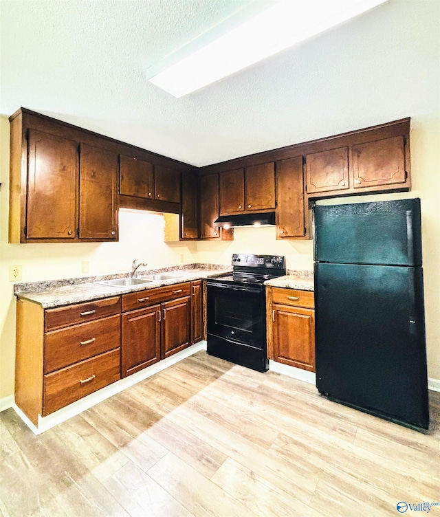 kitchen with a sink, black appliances, under cabinet range hood, light wood-style flooring, and light countertops