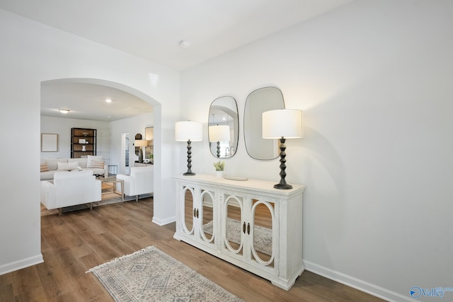 hall featuring baseboards, wood finished floors, and arched walkways