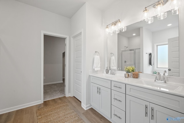 bathroom featuring wood finished floors, a sink, double vanity, and a stall shower