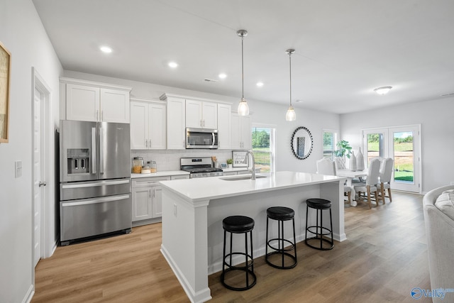 kitchen featuring a sink, stainless steel appliances, light wood-style flooring, a kitchen bar, and white cabinetry