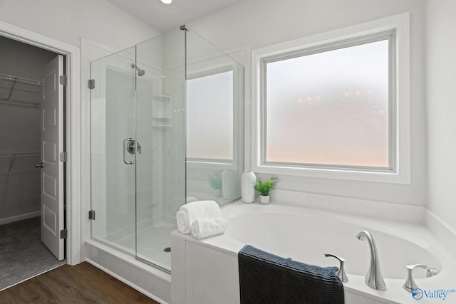 bathroom with a shower stall, a garden tub, a walk in closet, and wood finished floors