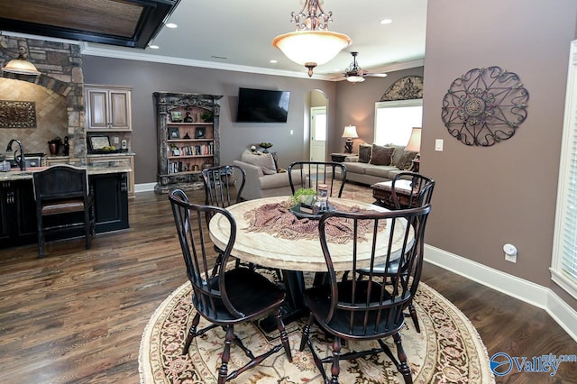 dining room with crown molding, baseboards, ceiling fan, arched walkways, and dark wood-type flooring