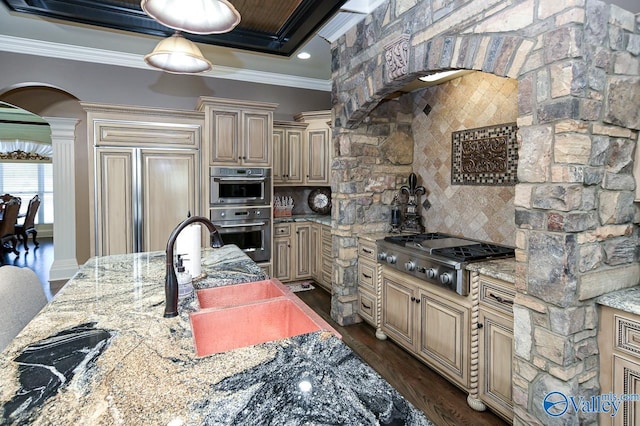 kitchen with a sink, cream cabinetry, stainless steel appliances, arched walkways, and ornate columns