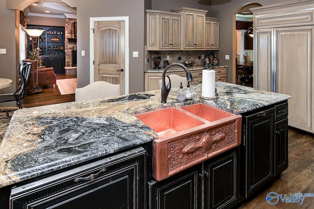 kitchen featuring dark wood finished floors, arched walkways, paneled built in fridge, a sink, and cream cabinets