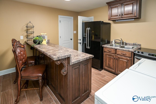 kitchen with a peninsula, stainless steel electric range oven, washer and dryer, a breakfast bar area, and black refrigerator with ice dispenser