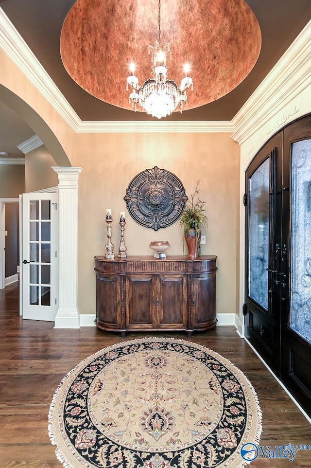 foyer entrance with ornate columns, an inviting chandelier, arched walkways, dark wood-style floors, and french doors