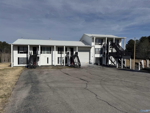 view of front of property with an attached garage, stairway, metal roof, and aphalt driveway
