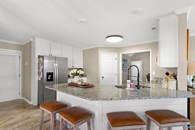 kitchen featuring white cabinetry, light stone counters, stainless steel fridge, and a sink