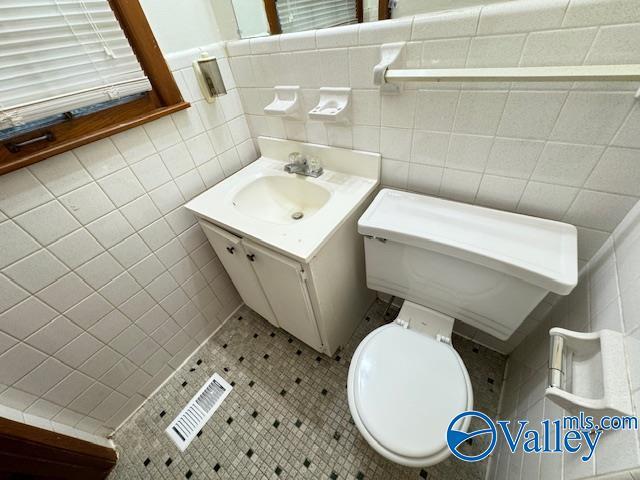 bathroom with visible vents, tile walls, toilet, and vanity