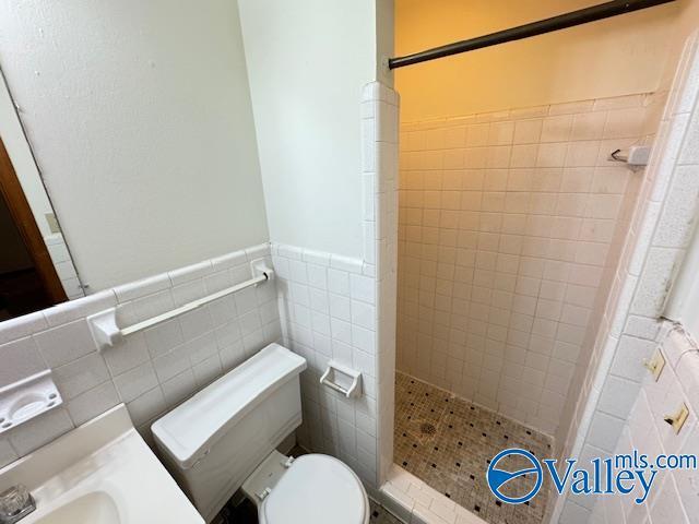 full bath with tile walls, wainscoting, a shower stall, and toilet