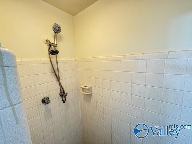 full bathroom with wainscoting, a tile shower, and tile walls