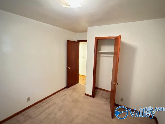 unfurnished bedroom featuring a closet, light colored carpet, and baseboards