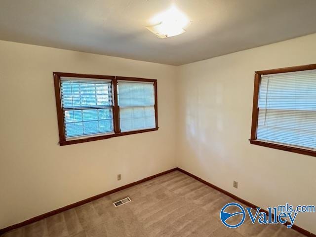 spare room featuring light carpet, visible vents, and baseboards