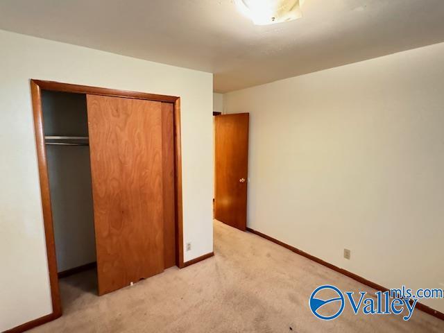 unfurnished bedroom featuring light carpet, a closet, and baseboards