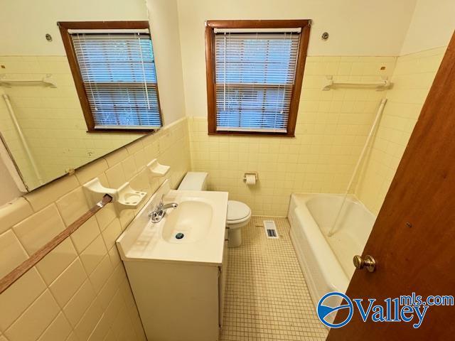 bathroom featuring toilet, tile patterned flooring, visible vents, and tile walls