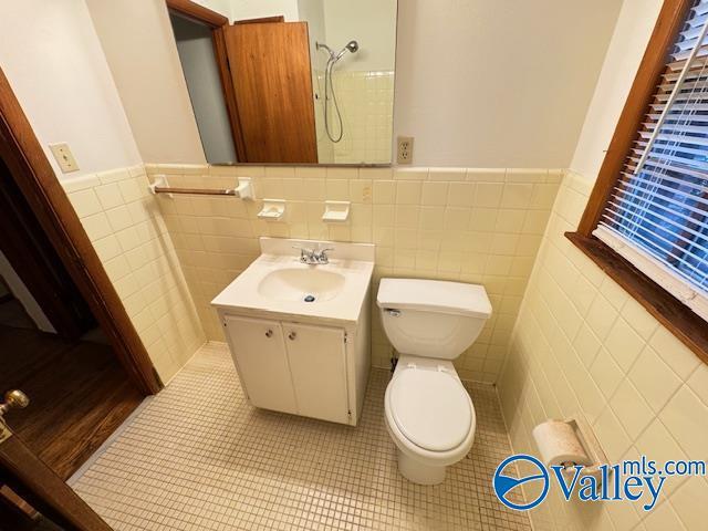 bathroom featuring toilet, a wainscoted wall, tile patterned floors, vanity, and tile walls