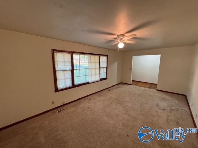 unfurnished room with carpet floors, visible vents, ceiling fan, and baseboards