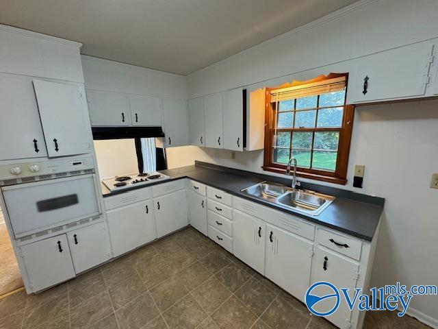 kitchen with dark countertops, white appliances, a sink, and under cabinet range hood